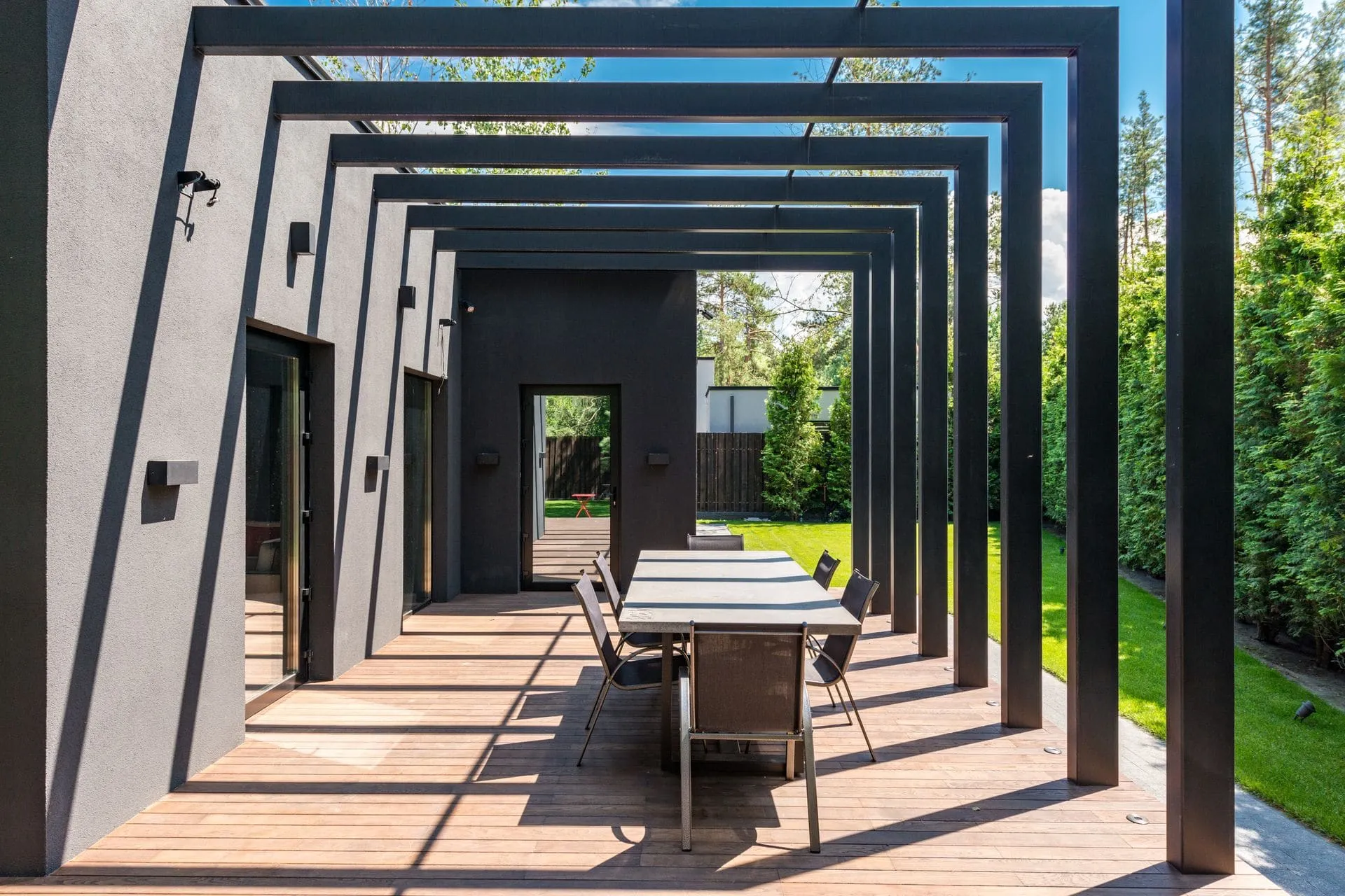 Black steel pergola over a timber deck and outdoor dining table, showing pergola cost factors