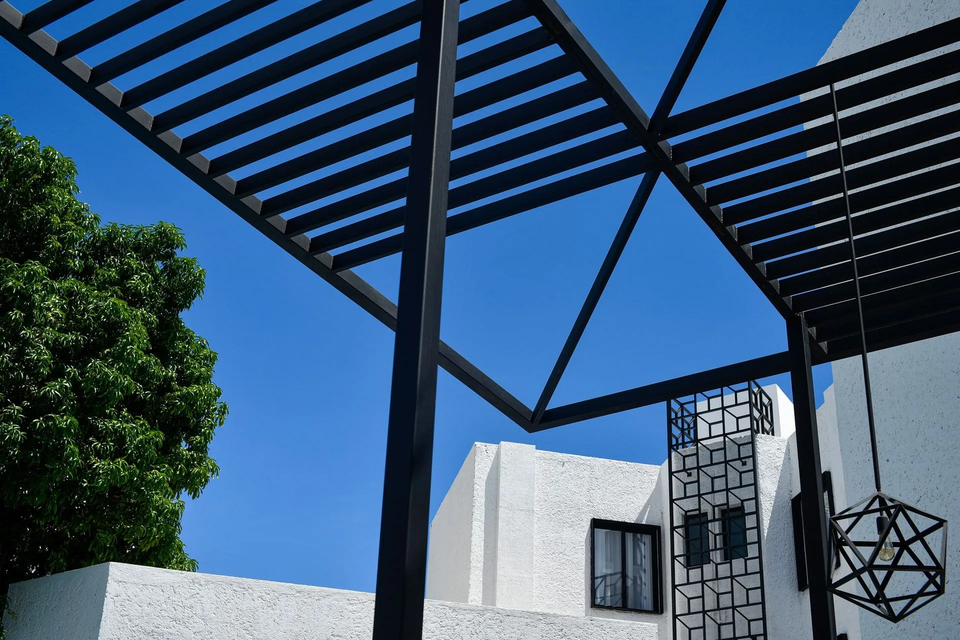 Black steel pergola frame with slim beams over an outdoor area against a blue sky